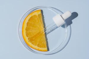 petri maträtt med orange skiva och kosmetisk pipett. hud vård citrus- syror forskning. hud vård Produkter testning foto