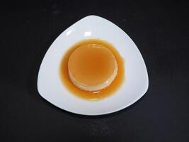 flan pudding eras i en maträtt isolerat på mörk bakgrund topp se foto