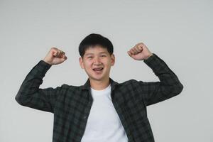 glad tonåring pojke med tandställning fira seger. glad asiatisk tonåring pojke med tandställning knäppning nävar i en triumferande gest på en grå bakgrund. porträtt stilig man i studio begrepp. foto