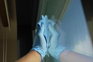 hand i blå handske rengöring fönster med grön trasa foto