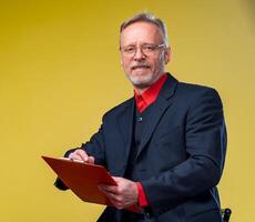 senior affärsman Sammanträde med mapp över gul bakgrund i kostym ser på kamera i röd skjorta . företag begrepp foto