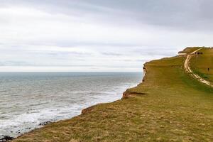 naturskön se av en gräs- klippa förbi de hav under en molnig himmel på sju systrar, england. foto