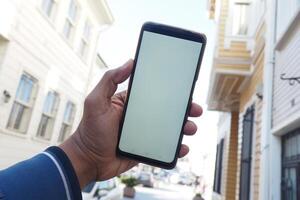 ung man hand använder sig av smart telefon med tömma skärm mot stad byggnader foto
