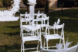 dekor på de bröllop. vit stolar dekorerad med vit blommor, på grön gräs. foto