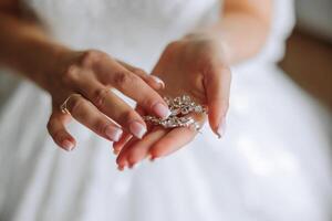 elegant brud innehav silver- örhängen. anbud händer med Smycken. ung brud sätter på henne bröllop dekoration foto