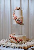 en stor lyxig flerdelad bröllop kaka är dekorerad med färsk rosa reste sig blommor i de bankett hall. bröllop efterrätt under de kväll ljus. bröllop dekor. foto