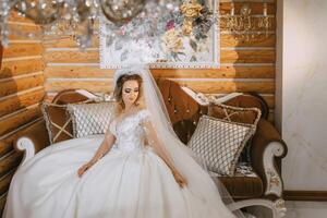 skön brud i en bröllop klänning med en skön frisyr i en skön trä- interiör, Sammanträde på en lyxig soffa foto
