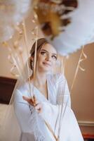skön brunett brud i en vit klänning, morgonrock, innehav vit gel bollar i henne händer och njuter henne bröllop dag i henne rum. bröllop fotografi. foto