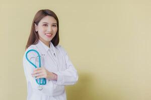 ung asiatisk kvinna läkare stående med vapen korsade självsäkert i sjukhus bär medicinsk enhetlig och stetoskop i de tema av hälsa kolla upp medan isolerat vit bakgrund. foto