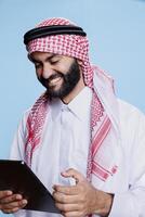 arab man skrattande medan njuter internet underhållning aktivitet på digital läsplatta. leende muslim person har roligt medan chattar uppkopplad och rullning social media på grej pekskärm foto