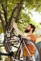 fokuserade ung manlig cyklist ser till cykel är väl förberedd för utomhus- äventyr förbi flitigt säkring däck sudd. friska och aktiva man innehav cykel hjul för underhåll. foto