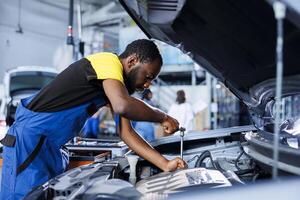 specialist i bil service användningar vridmoment rycka till spänna skruvar efter byter ut motor. afrikansk amerikan skicklig bil reparera affär anställd användningar professionell verktyg till fixera kund bil foto