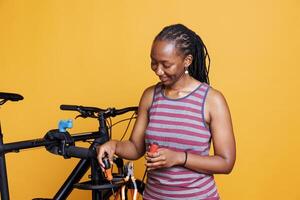 ung afrikansk amerikan lady framställning grundläggande verktyg för lagning skadad cykel. sportig svart kvinna gripa tag i flera specialiserade Utrustning för reparation bruten cykel mot ett isolerat bakgrund. foto