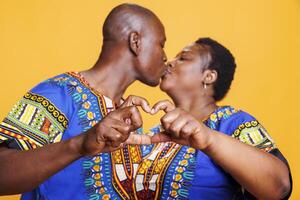 afrikansk amerikan par kissing i mun och som visar hjärta form med fingrar. romantisk svart man och kvinna partners uttrycker tillgivenhet medan framställning kärlek gest tillsammans foto