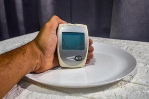 hand innehav en testa verktyg för blod glukos, kolesterol och urin syra nivåer på en middag tallrik foto