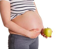 gravid kvinna stående och innehav äpple nära henne mage foto