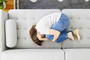 frustrerad kvinna beläggning ansikte och gråt, liggande på soffa på Hem ensam foto