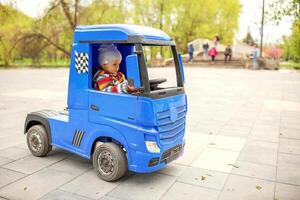 söt liten pojke körning elektrisk leksak bil utomhus i parkera. foto