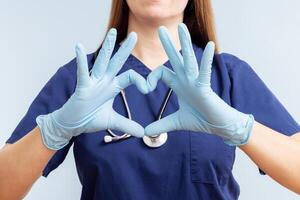 läkare kvinna i handskar håller på med hjärta symbol form med händer på blå bakgrund foto