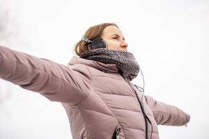 glad ung kvinna i jacka lyssnande till musik, avkopplande i en parkera foto