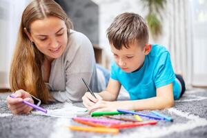 Lycklig familj spelar tillsammans på golv. mor och son målning tillsammans foto