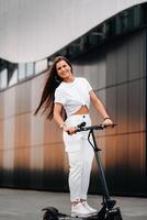 skön flicka i vit eleganta kläder på ett elektrisk skoter i de stad foto