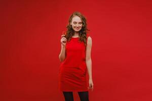 en skön flicka i en röd klänning på en röd bakgrund innehar en jordgubb i henne händer och ler foto