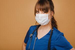 en flicka läkare står i en medicinsk mask, isolerat på en brun bakgrund foto