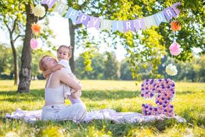 glad mor och dotter har roligt på barn födelsedag på filt med papper dekorationer i de parkera foto