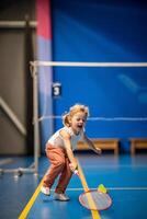 liten flicka tre år gammal spelar badminton i sport ha på sig på inomhus- domstol foto