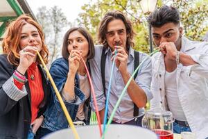 grupp av mångkulturell vänner har roligt på de trädgård fest sugande öl från färgrik strån foto