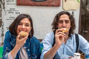 leende skön par äter pizza utomhus se på kamera foto