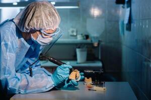 en dental tekniker i skyddande Kläder är arbetssätt på en protes- tand i hans laboratorium foto