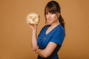 söt ung läkare flicka innehav en mänsklig skalle, brun bakgrund Bakom de läkare foto
