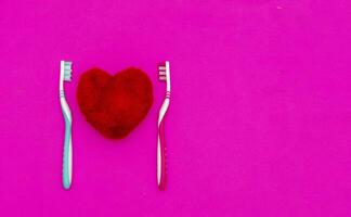 röd hjärta mellan två tandborstar på pastell rosa bakgrund. manlig och kvinna tänder hygien begrepp. stänga upp. tömma plats för härlig, söt text, Citat eller ord foto