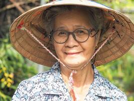 porträtt av en senior asiatisk kvinna bär en hatt, leende och ser på de kamera medan stående i en trädgård. Plats för text. begrepp av gammal människor och sjukvård foto
