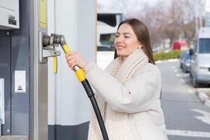 ung kvinna innehav en bränsle munstycke i henne hand medan tankning bil på gas station. en sluta för tankning på de gas station. bränslen de bil med gas. foto