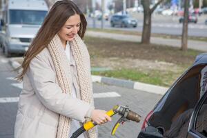 ung kvinna innehav en bränsle munstycke i henne hand medan tankning bil på gas station. en sluta för tankning på de gas station. bränslen de bil med gas. foto