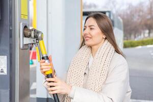 ung kvinna innehav en bränsle munstycke i henne hand medan tankning bil på gas station. en sluta för tankning på de gas station. bränslen de bil med gas. foto