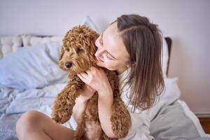 ung kvinna spelar och kissing cockapoo flicka på säng, minimalism foto