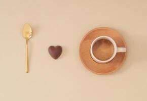 jag kärlek kaffe. kreativ sammansättning tillverkad med gyllene sked, choklad hjärta och kopp av kaffe på pastell beige bakgrund. minimal begrepp. trendig kaffe med kärlek aning. platt lägga. foto