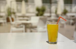 glas av orange juice med plast sugrör på vit tabell i restaurang utomhus- vardagsrum zon foto