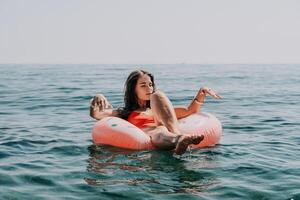 kvinna sommar hav. Lycklig kvinna simning med uppblåsbar munk på de strand i sommar solig dag, omgiven förbi vulkanisk berg. sommar semester begrepp. foto