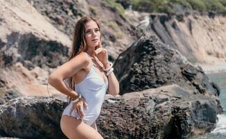 kvinna resa hav. Lycklig turist i vit bikini njut av tar bild utomhus för minnen. kvinna resande Framställ på de strand på hav omgiven förbi vulkanisk berg, delning resa äventyr resa foto