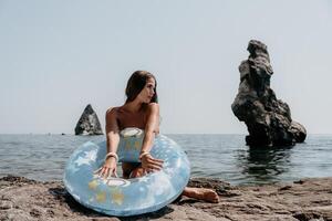 kvinna sommar hav. Lycklig kvinna simning med uppblåsbar munk på de strand i sommar solig dag, omgiven förbi vulkanisk berg. sommar semester begrepp. foto