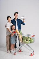 bild av asiatisk familj tryckande en mataffär vagn medan handla, isolerat på vit bakgrund foto