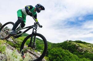 professionell cykling. utför härkomst från de bergen förbi cykel. ung ryttare gående ner de berg på en berg cykel i sommar omgiven förbi grönska foto