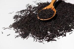 torr svart te löv i en trä- sked, vit bakgrund. lugg av spridd te löv. foto