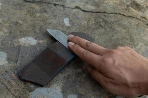 kniv skärpning på kniv skärpning sten. bakgrund av cement golv och hand innehav kniv skärpning. foto