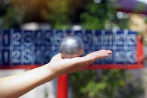 spelare håll en petanque boll i deras händer och förbereda till kasta den i beställa till plats de petanque boll som stänga till de mål boll som möjlig. foto